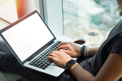  close up of woman hands typing on keyboard. young casually dressed female freelancer working home sitting on windowsill. laptop with blank white screen. mock up, copy spzce for your text.
