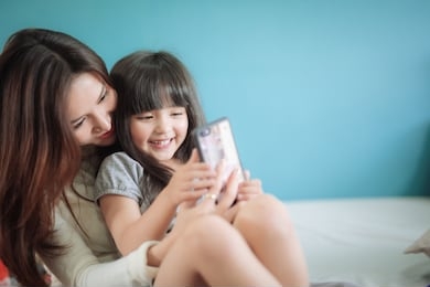 portrait happy daughter playing smartphone with her mother