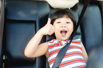 smiling asian child girl thumbs up for good drive good trip and safe on the road. sitting and buckle up in the car in the seat for children.