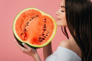 beautiful smiling girl with closed eyes holding ripe delicious watermelon half isolated on pink