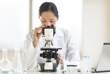 mid adult asian female doctor using microscope at desk in laboratory