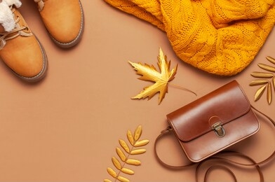 brown leather women bag, orange knitted sweater, warm boots, golden autumn leaf on brown background top view flat lay. fashionable women's accessories. autumn fashion concept. stylish lady clothes 