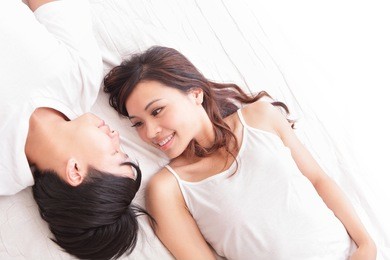 young lovely couple lying in a bed, happy smile looking to each other, top view, asian people