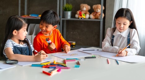 group of asian child little drawing with colourful pencils crayons in classroom.
