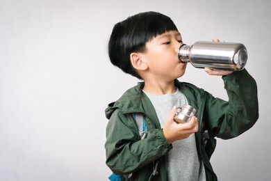 studio portrait: adorable little asian boy drinks water from stainless steel reusable water bottle. eco friendly lifestyle, reduce single use plastic, no straw, green living, world water day.