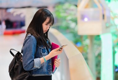 portrait of young asian female student using her mobile phone sending a text outside