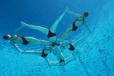 underwater view of synchronized swimmers forming a star shape in pool