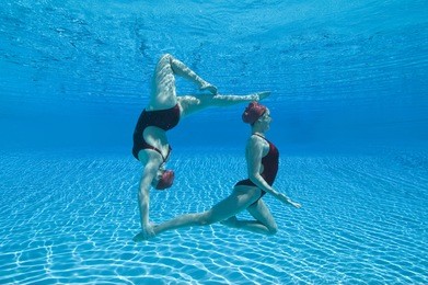 full length side view of two synchronized swimmers performing underwater