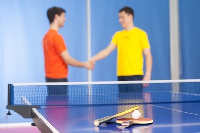 good game! two young men in sports clothing handshaking near the tennis table