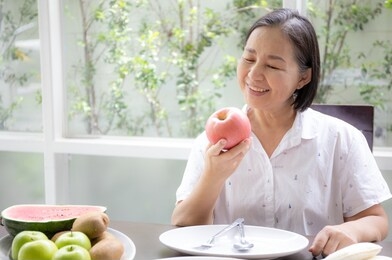 old woman or elder sitting and happy or enjoy eating with apple fruit, healthy life 
