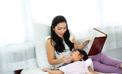 happy little girl looking at book with her mother