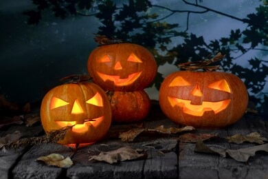 three halloween pumpkins head jack o lantern on wooden table background in a mystic  forest at night. halloween design with copyspace.
