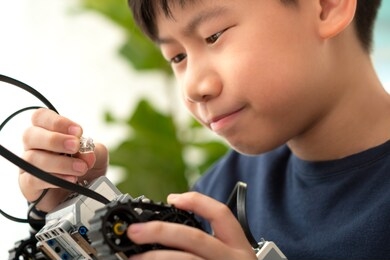 closeup: smart looking preteen / teenage asian boy learning and looking at connector cable with curiosity and passion. stem education, science, technology, engineering, programming, robotics project.
