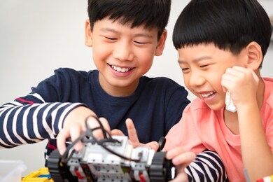 cheerful preteen / teenage asian brother assembles and shows his robotics project to cute little boy. two brothers laugh, smile, have fun. family activity, quality happy time, brotherhood bonding.