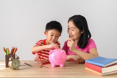 asia boy and his mother with piggy bank on  table and white wall. child saving money for school education whith copy space concept.
