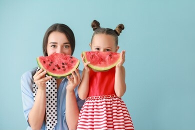 beautiful young woman and cute little girl with fresh watermelon on color background