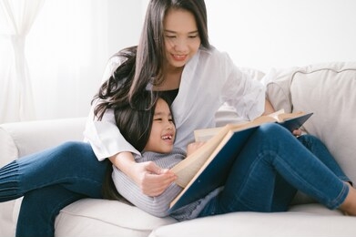 happy child little asian girl  reading a books on the table in the living room at home. family activity concept