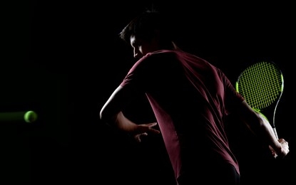 young tennis player ready to hit the ball isolated on a dark background