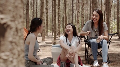 group of young asian friends camping or picnic together in forest, teenager female enjoy moment talking in front of their tent. women do adventure activity and travel on holidays vacation in summer.