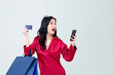 surprised young asian woman shopping online with smartphone and paying by credit card on gray studio background