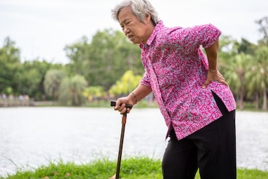 asian senior woman with hip joint pain while walking,female patient having backache,lumbago pain,hands touching on the hip in outdoor park,elderly people suffering from ribbing pain or waist pain