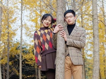 portrait of chinese young lovers standing together and smiling at camera with golden autumn forest background, romantic lovers concept.