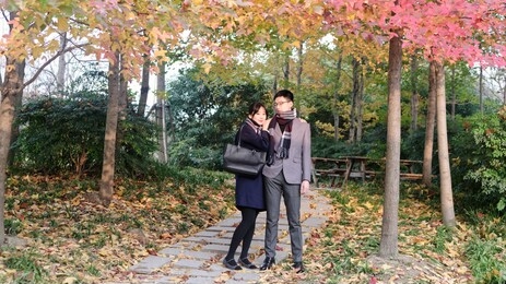 portrait of a beautiful chinese young woman hugging her boyfriend's shoulder in autumn forest park, warm sunlight lighting their face, romantic moment.