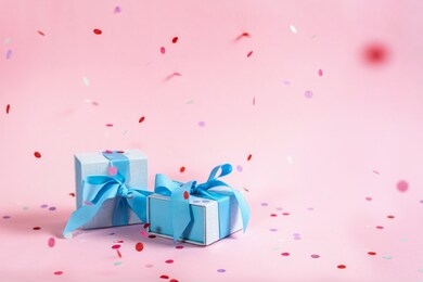 party time concept! two beautiful and blue wrapped present or gift box with ribbon isolated against shine pink background with copy or empty space for text with paper and colorful confetti decorations