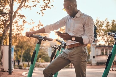 young african guy is paying for electrical scooter by web payment using his mobile phone.