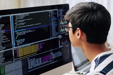 smart teenage boy in glasses checking programming code on computer screen when sitting at his desk