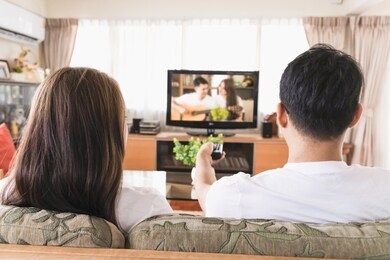asian male and female couples are watching tv on the sofa in the house.