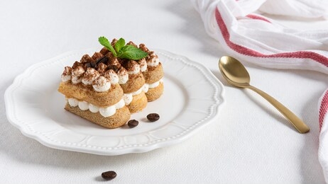 traditional italian dessert tiramisu with cocoa powder, mint and coffee beans on white plate on white background. for menu, confectionery, cafe. copy space