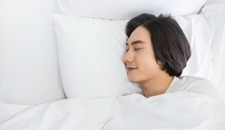 portrait of handsome young asian man with enjoy fresh soft bedding linen mattress in white bed room modern retro apartment. asian guy sleep resting, good night sleep concept panoramic banner