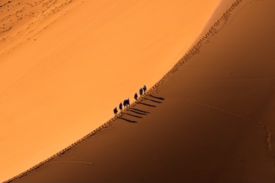 aerial view group of people walking on the sand dune in the desert and sun gradually create beautiful scene.