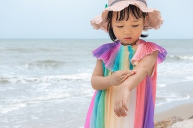 child applying sunscreen on the beach during summer vacation,kid girl applies sun protection cream on the skin. children, summer and healthcare concept