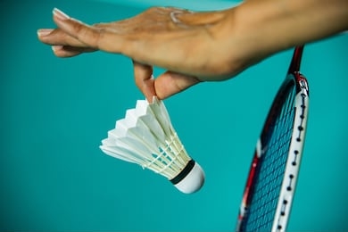 closeup hands of woman badminton player holding shuttlecock and racket ready to serve with green blur badminton court background, most popular sport in south east asia.