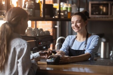 female customer holding phone near nfc terminal make contactless mobile payment with smiling waitress barista saleswoman on coffeeshop counter, woman client pay in cafe with cellphone via pos machine