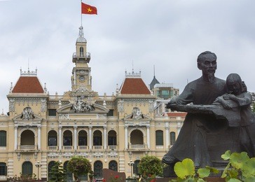 ho chi minh statue and saigon city hall with flag. combination shot of the statue with the chateau-like french-built city hall, the center of power in ho chi minh city.