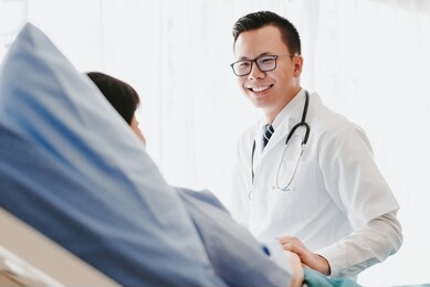 asian doctor giving his female patient a thorough checkup during his consultation on the bed in hospital
