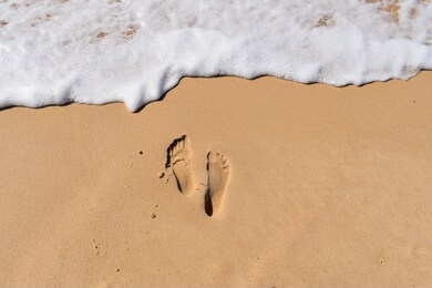 feet in the sand being washed up by the sea