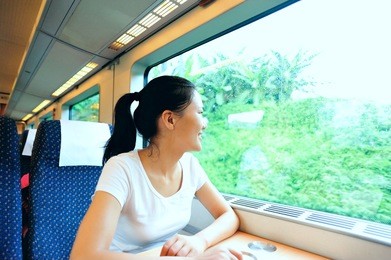 young asian woman looking out of the window smiling interior of train/subway 