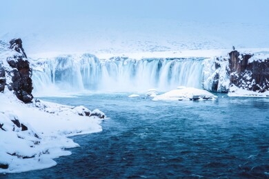 the godafoss or water of gods is a big waterfall located in northeastern region in iceland,europe. there is a photographer standing with his camera.