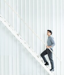 young asian businessman walking up the stair confidently.  achievement and motivation in employment and life concept with copy space backgound.
