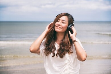 a beautiful asian woman enjoy listening to music with headphone by the sea