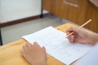 english exams test student in school, university students holding pencil for testing exam writing answer sheet or exercise for taking in assessment paper on table classroom. education study concept