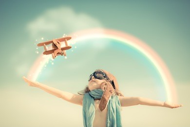 happy kid playing with toy airplane against summer sky background