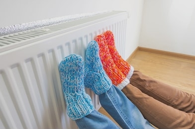 family in warm knitted woolen socks near a home heater in cold winter time. the symbolic image of the heating season at home. part of body, selective focus.