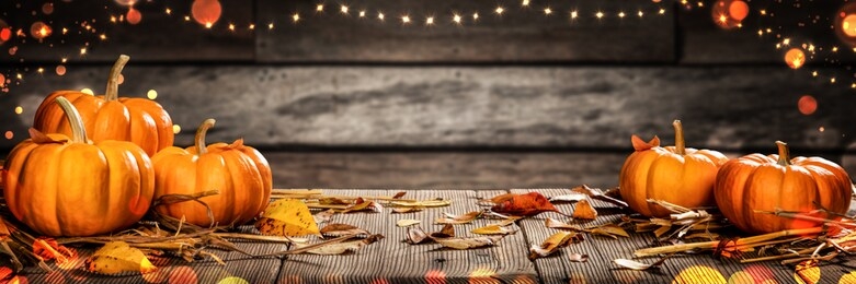mini thanksgiving pumpkins and leaves on rustic wooden table with lights and bokeh on wood background - thanksgiving / harvest concept