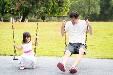 asian father and daughter are playing the swing together in the playground of the park with happy moment, concept of outdoor activity for children in the family lifestyle.