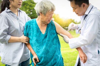 male asian doctor with syringe doing injection vaccine,flu,influenza in the shoulder of senior woman,family doctor injecting,vaccinating elder patient in park,vaccination,medicine,health care concept